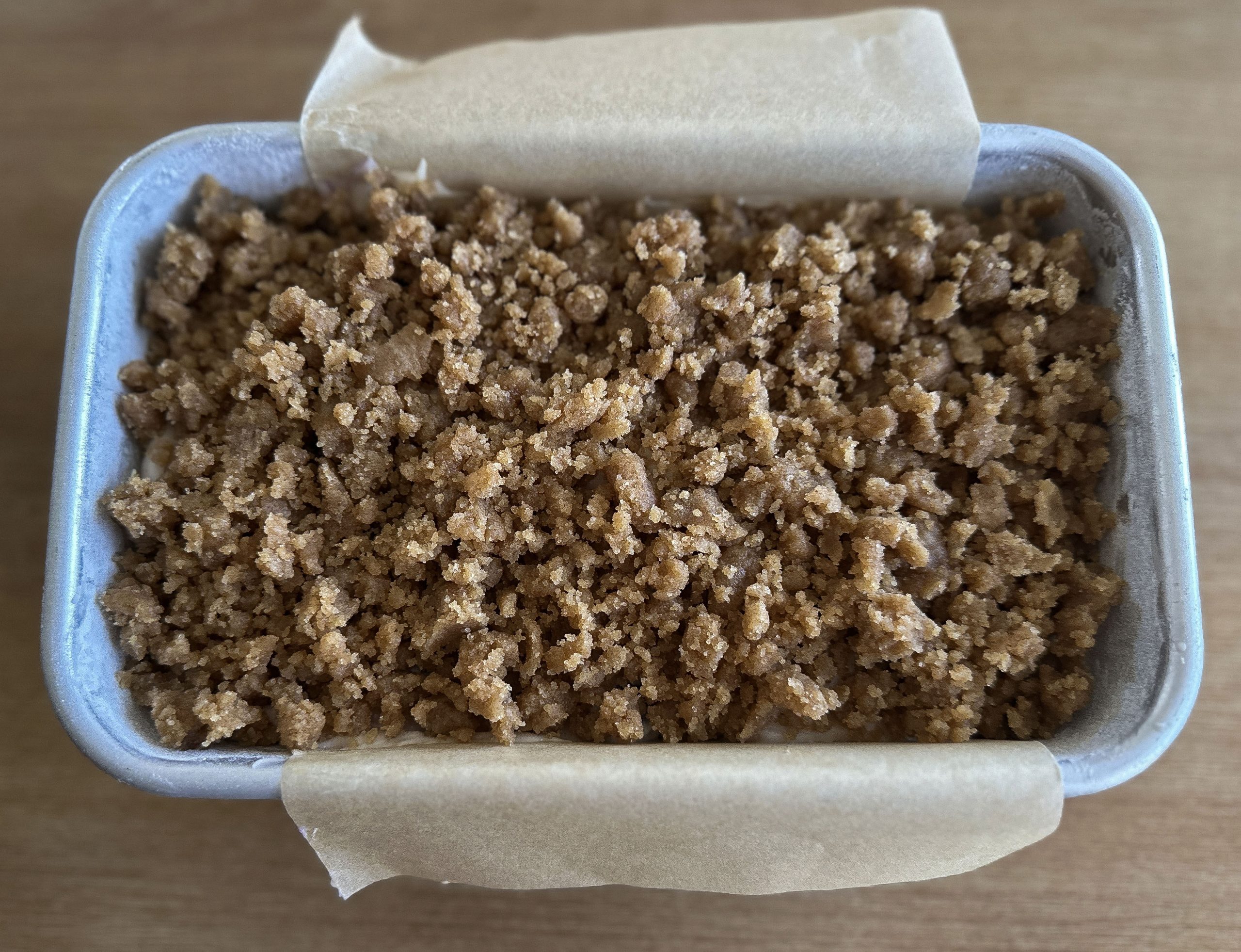 Unbaked blueberry sour cream loaf in a parchment-lined pan, topped with a thick layer of brown sugar streusel before baking.