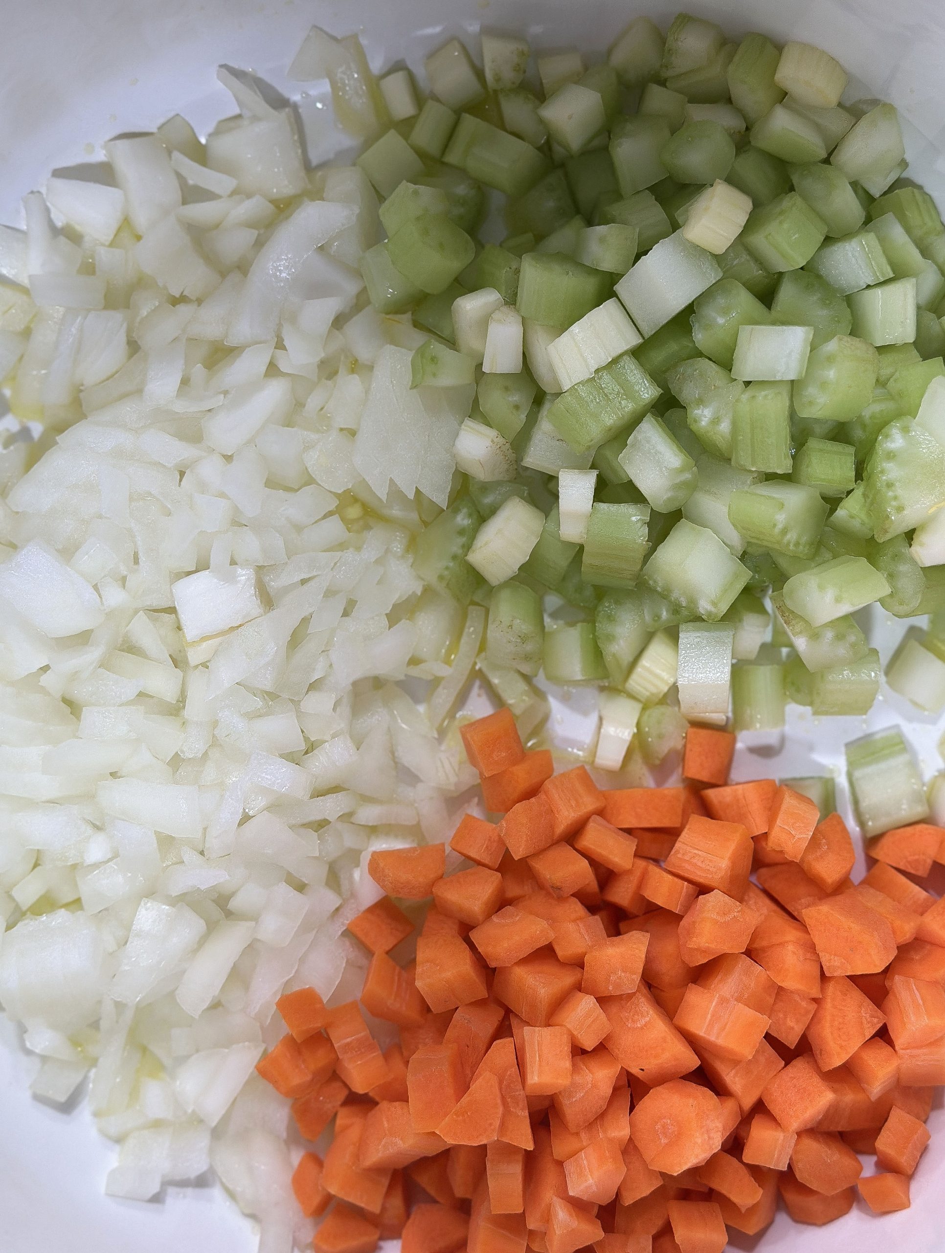 A close-up of diced onions, celery, and carrots, prepped and ready for cooking in a minestrone soup.