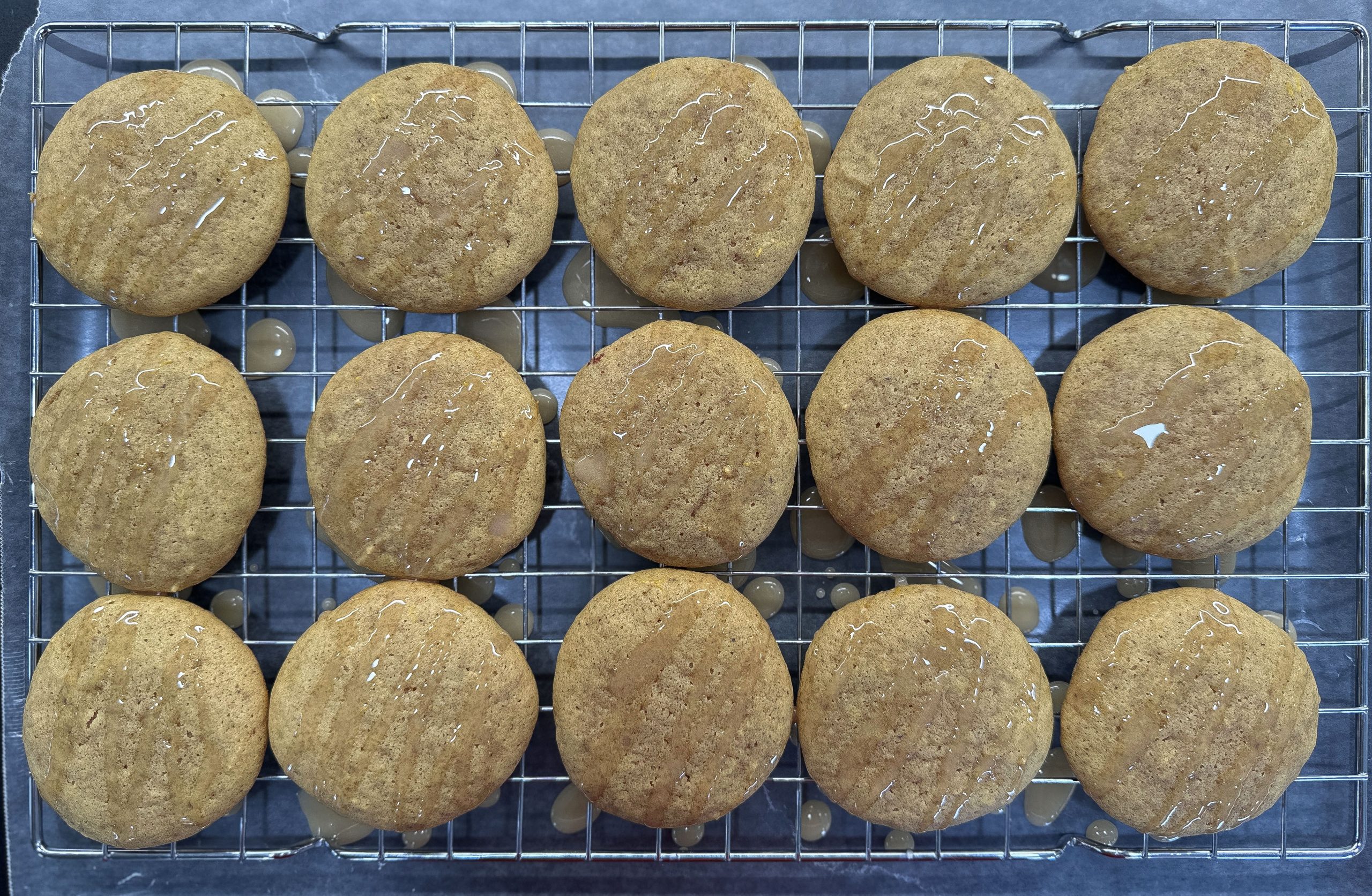 This image shows freshly baked pumpkin spice cookies cooling on a wire rack, with a light drizzle of glaze on top, allowing excess glaze to drip beneath.