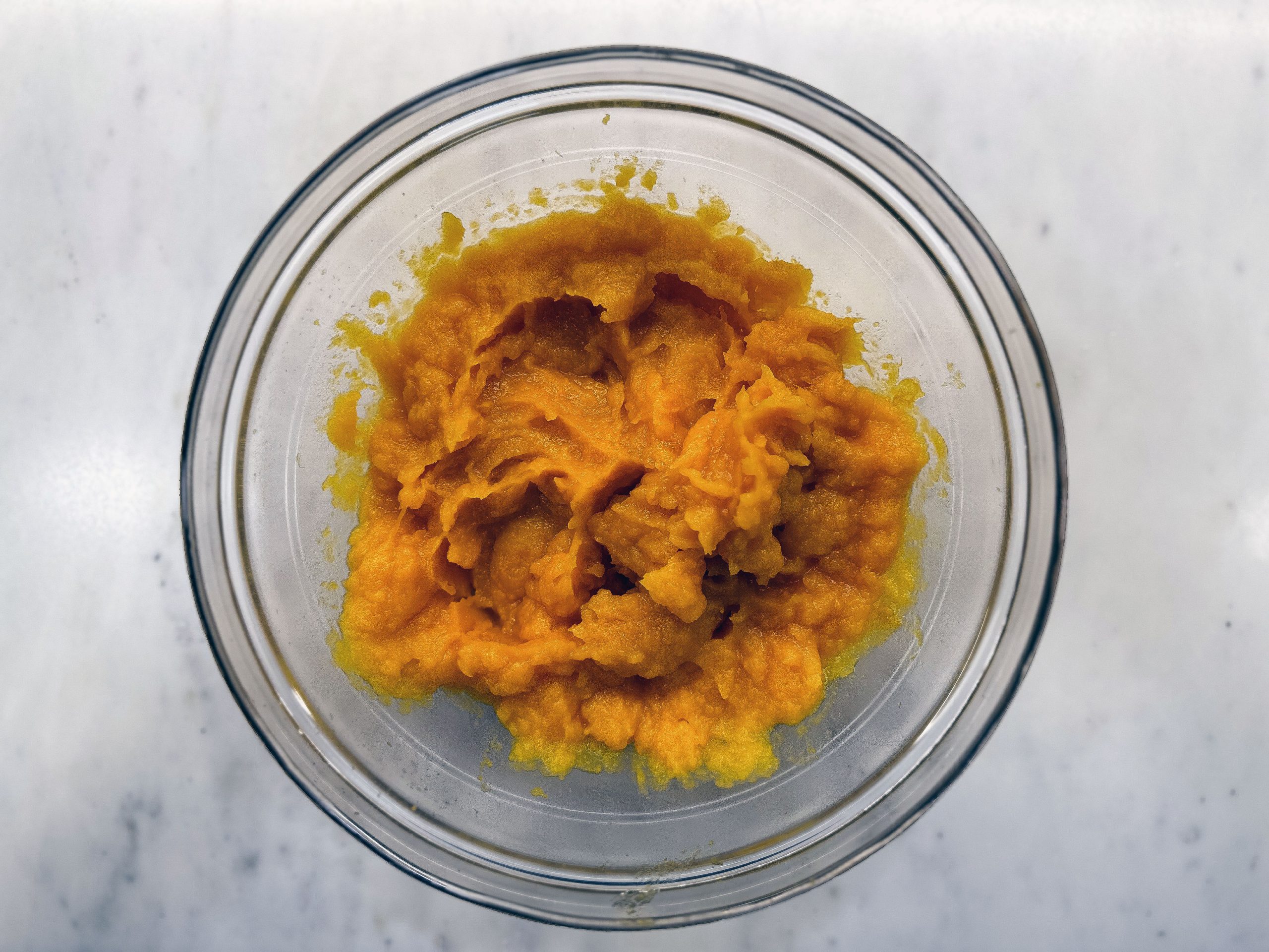 This image shows a glass bowl filled with smooth, bright orange pumpkin puree, placed on a light-colored surface.