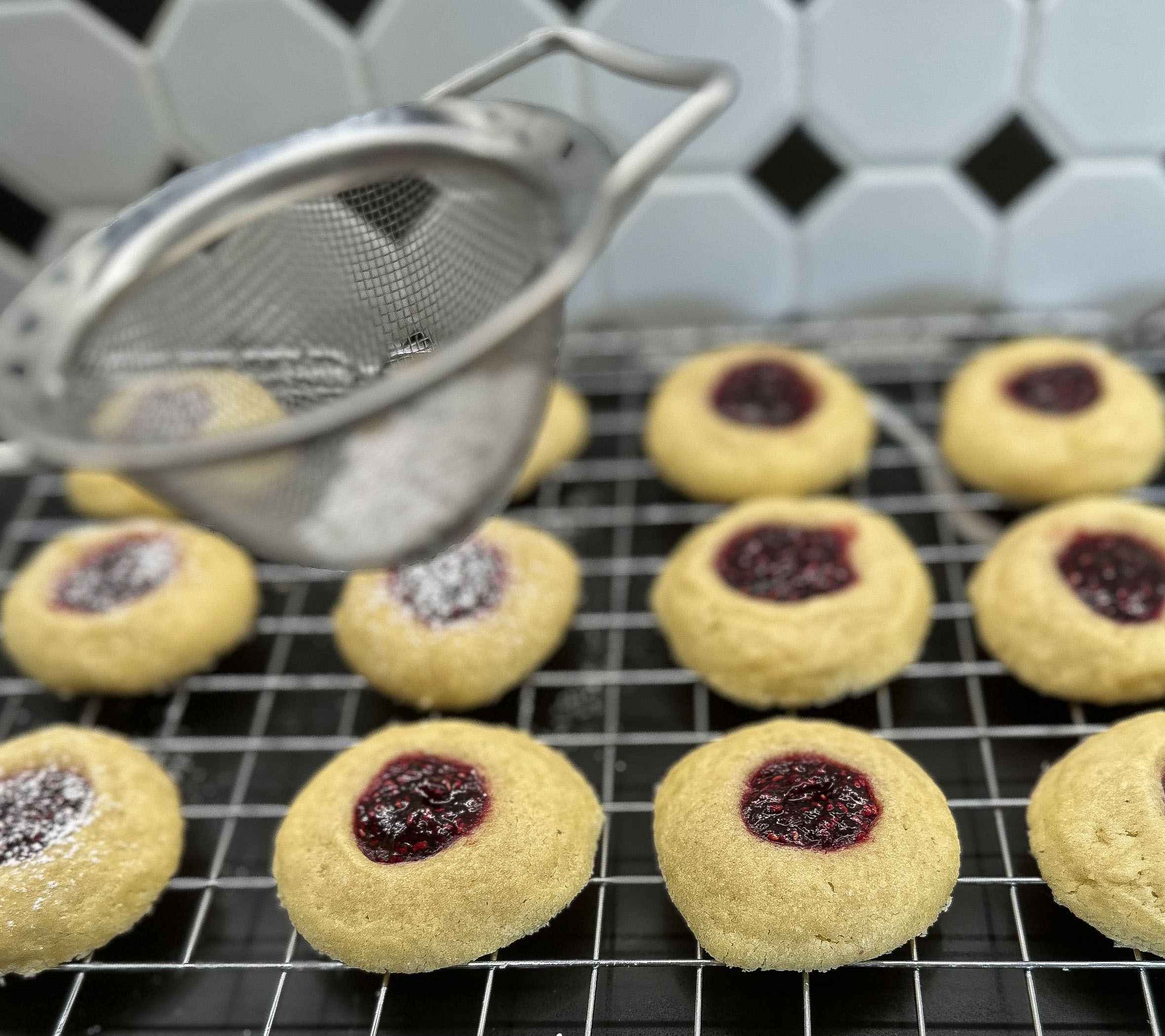 Freshly baked raspberry thumbprint cookies being dusted with powdered sugar.