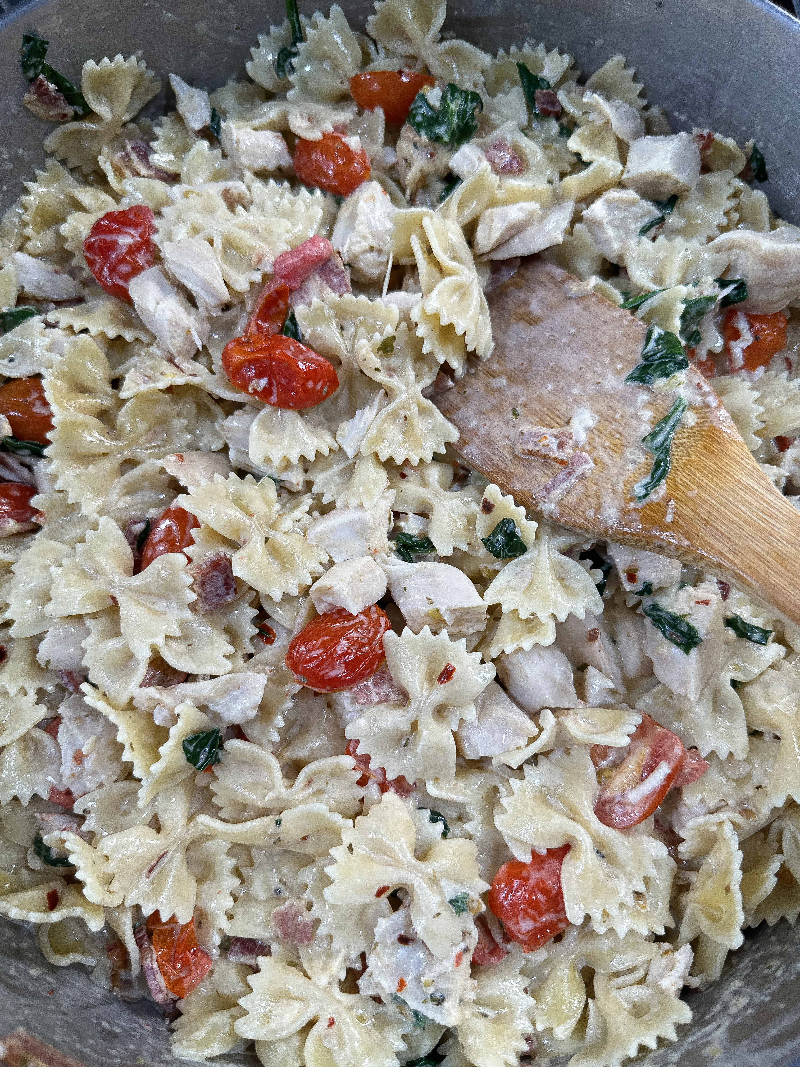 Creamy bow tie pasta with chicken and bacon, mixed with cherry tomatoes and spinach in a rich Parmesan sauce, ready to be served.