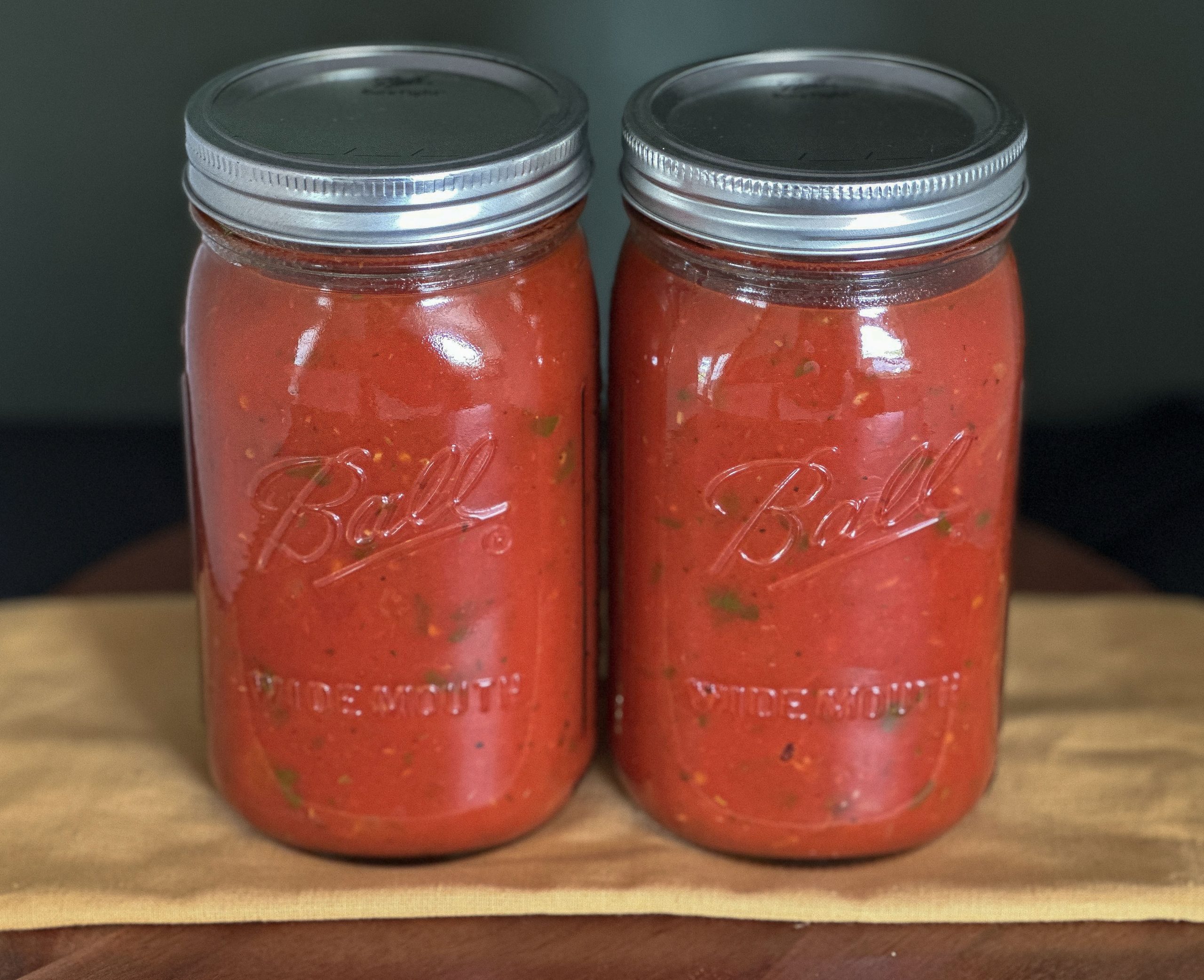Two Ball wide-mouth jars filled with homemade marinara sauce, placed side by side on a wooden surface with a yellow cloth underneath.