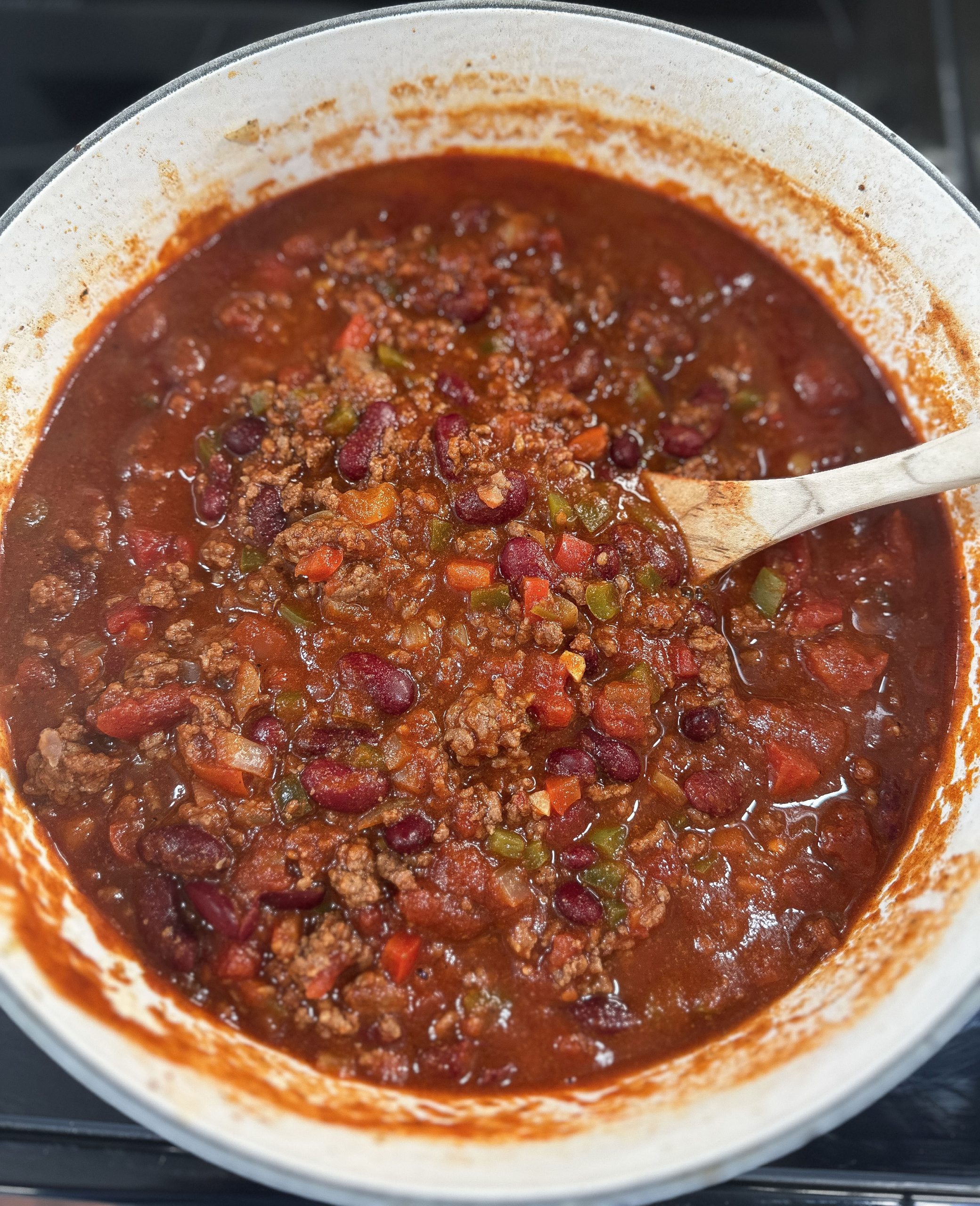 A pot of classic homemade chili simmering with ground beef, kidney beans, and vegetables, stirred with a wooden spoon.