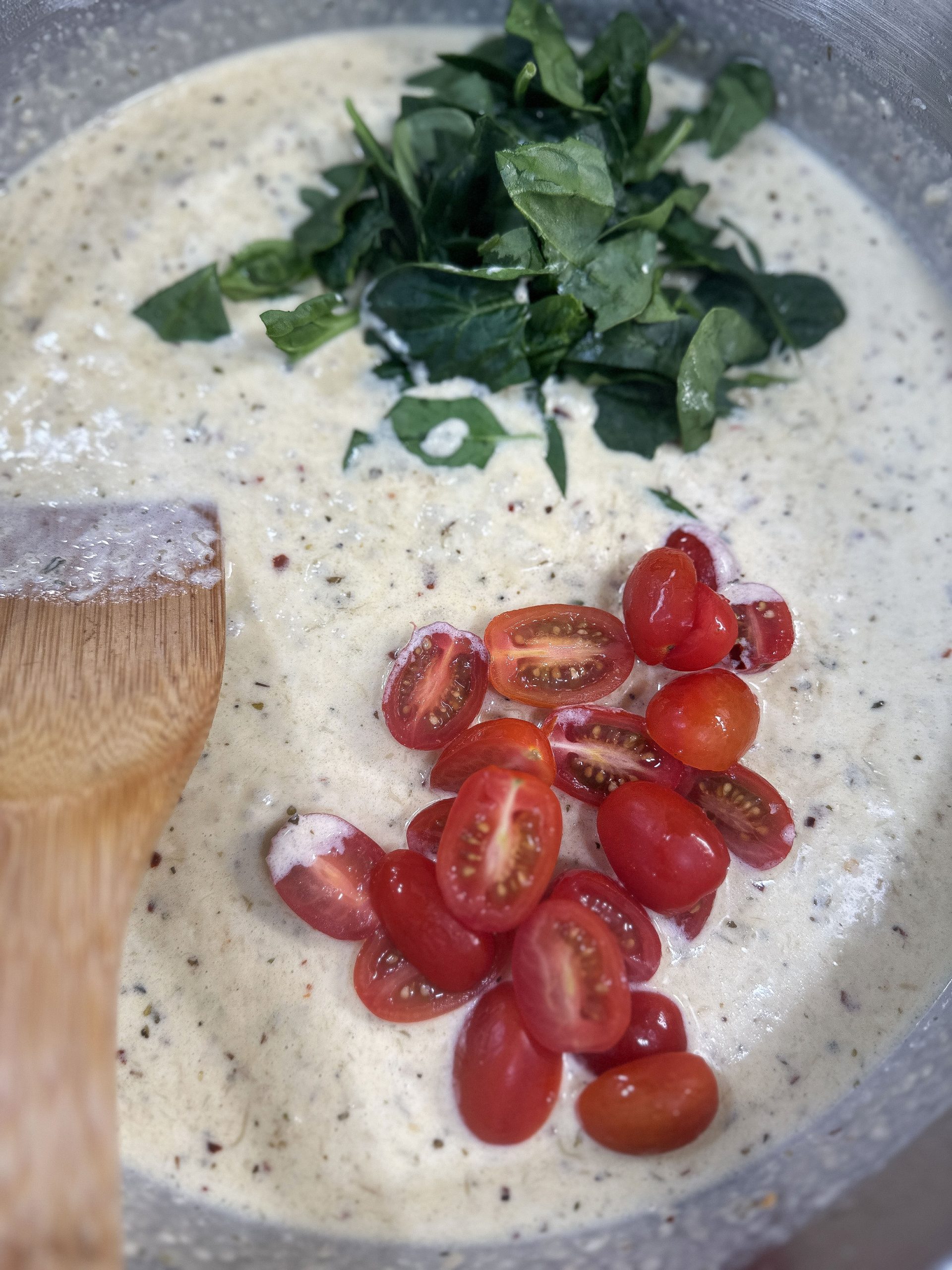 Fresh spinach and halved cherry tomatoes being added to the creamy pasta sauce in a pan.